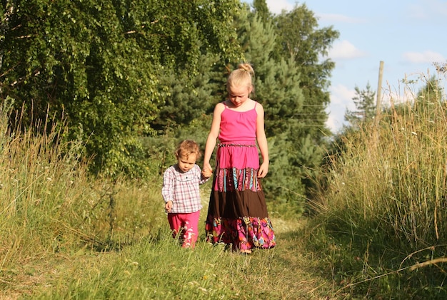 Two adorable little girls walking on the green field at summer