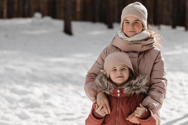 Two adorable young girls having fun together by beautiful frozen park forest Cute sisters playing in a snow