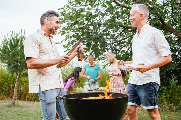 Two adult friends or family men talking and smiling cooking and grilling in a barbeque party