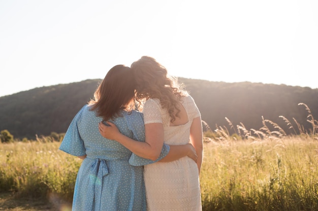 Two adult girlfriends hug each other at the background of nature