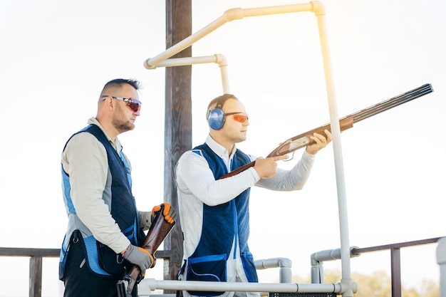 Two adult mans in sunglasses and a rifle vest practicing fire weapon shooting