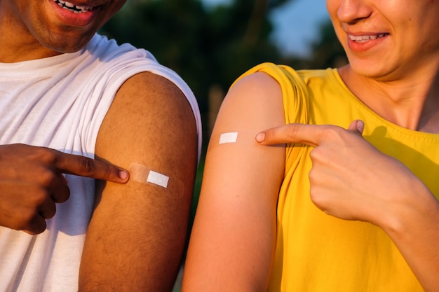 Two african american and caucasian friends showing their hands after vaccination