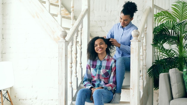 Two african american curly girls sistres make fun curly hairstyle each other and have fun at home