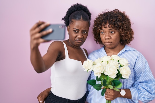 Two african women taking a selfie photo with flowers skeptic and nervous, frowning upset because of problem. negative person.