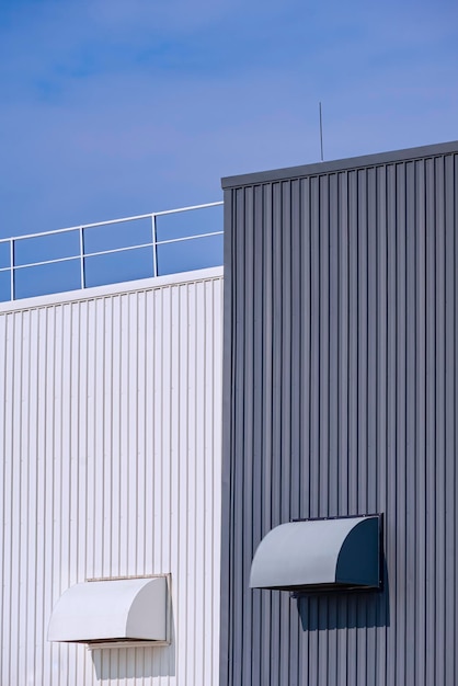 Two air ducts ventilation on grey and white corrugated metal factory buildings wall with blue sky