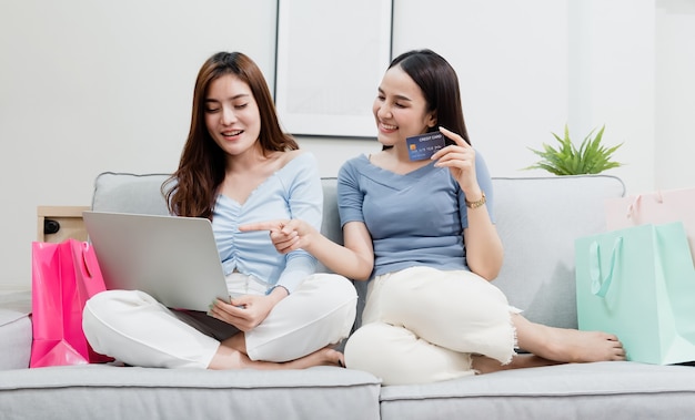 Two Asian beauty  people are using a credit card to make purchases using a laptop via the internet. With a happy smiling face, being a new normal online business In the shopping experience from home