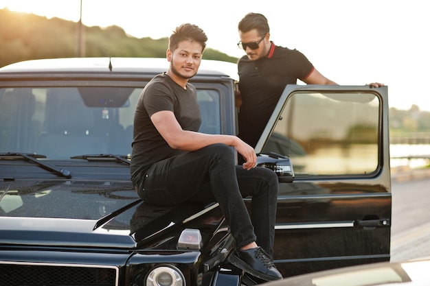 Two asian brothers man wear on all black posed near suv car.