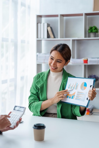 Two Asian business colleagues using calculator and discussing new project while brainstorming together at desk in office workplace