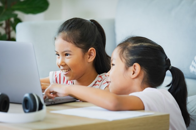 Two asian child girl students study online with teacher by video call together. Siblings are homeschooling with computer laptop during quarantine due to Covid 19 pandemic.