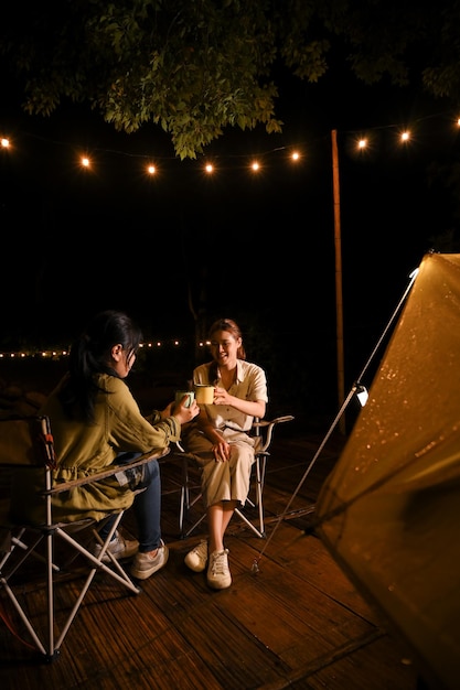 Two Asian female best friends talking sipping hot coffee and enjoy camping together at night