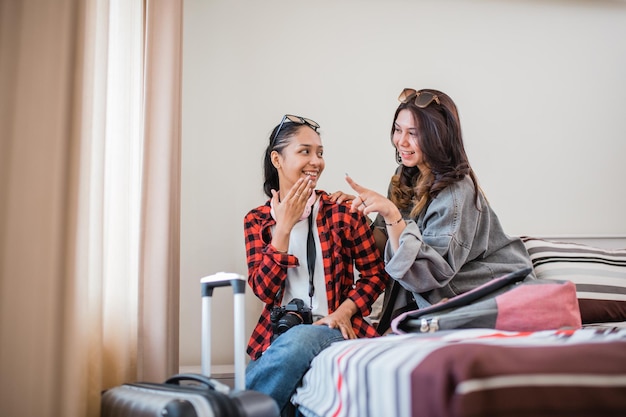 Two asian female travelers chat while sitting on a hotel room bed