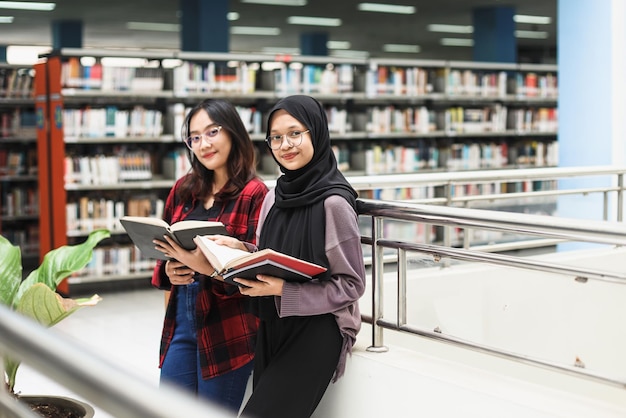 Two Asian students in casual style smiling while opening a book against blurred library background