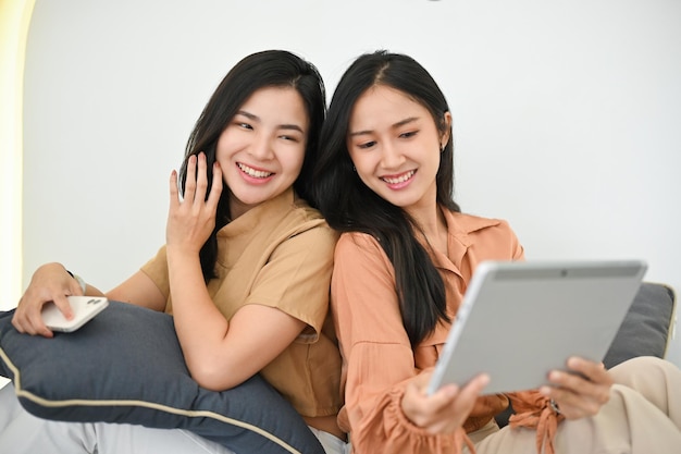 Two asian young female best friend sitting leaning on each other using tablet