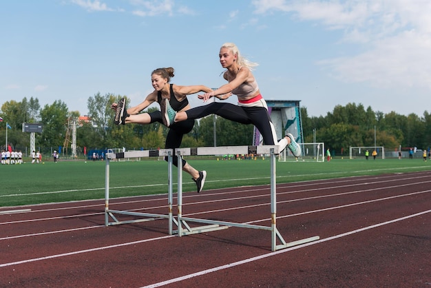 Two athlete woman runnner running hurdles at the stadium outdoors