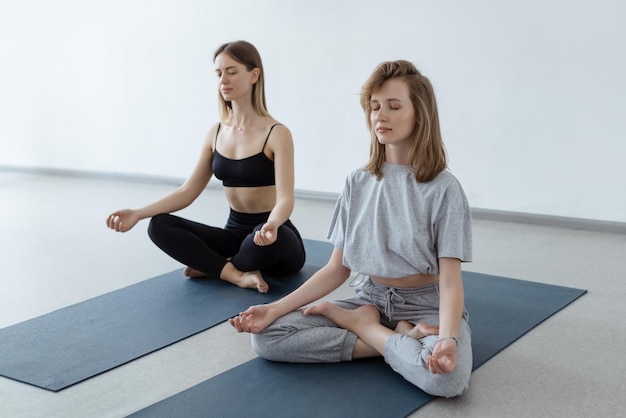 Two athletic attractive girls sit in lotus position on yoga mat indoors Yoga fitness and healthy lifestyle