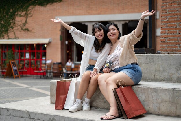 Two attractive Asian female friends are sitting on the stairs in the city with their shopping bags