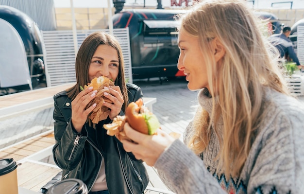 Photo two attractive european women eat street fast food while sitting at a table outside