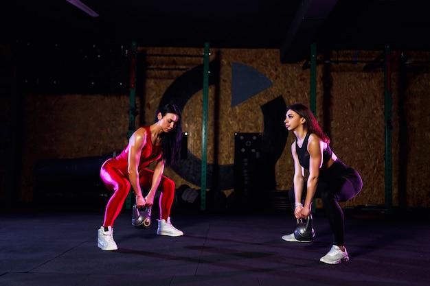 Two Attractive fit women athlete performing a kettle-bell swing in gym