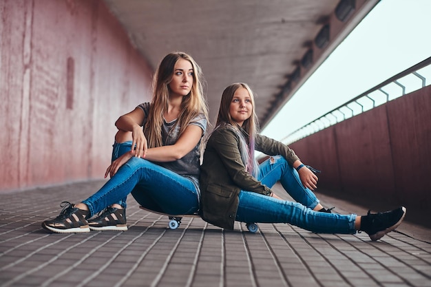 Two attractive friendly teenagers are sitting on the skateboard in long tunnel.