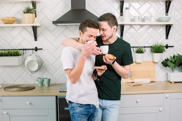 Two attractive guys are drinking coffee. Two handsome homosexual men at home kitchen. Comfort and relaxation.