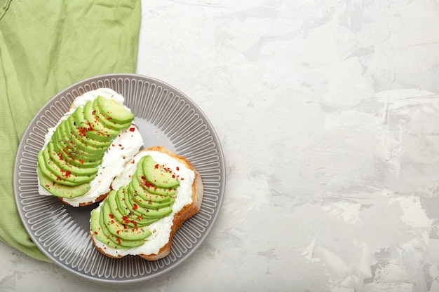 Two avocado toasts, avocado sandwich. Fresh avocado sliced on toast of wheat bread, cream cheese. Avocado sprinkled with chili, basil spices on a gray concrete background with place for text, top view