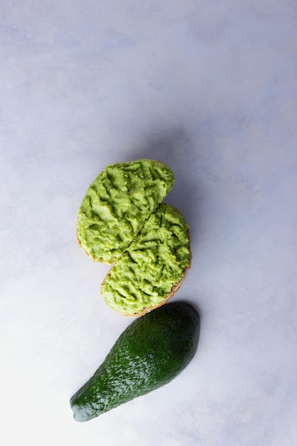 Two avocado toasts and half a fresh ripe avocado isolated on white background Healthy breakfast food Vegetarian food concept Closeup View from above