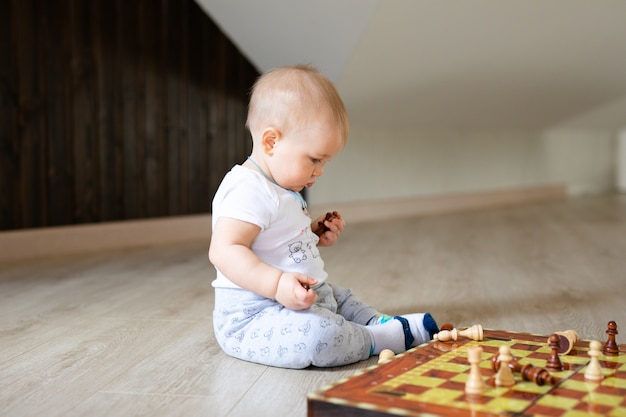 Two babies boy and girl playing chess on the white wooden floor at home.