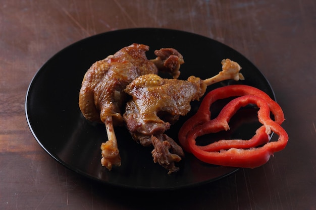 Two baked duck legs on a black plate with red bell pepper on a dark background Delicious duck legs with a golden crust closeup