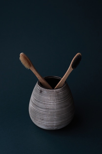 Two bamboo toothbrushes in a porcelain glass on a cyan gradient background