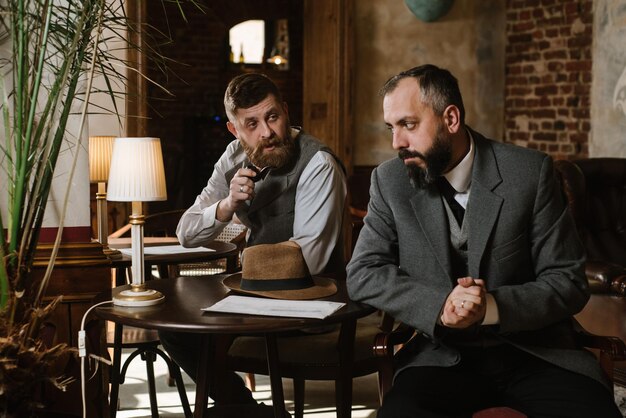 Two bearded men wearing old fashioned suits talking or discuss something in the restaurant