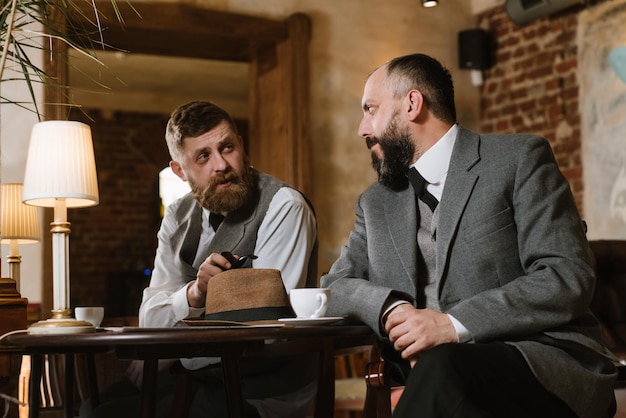 Two bearded men wearing old fashioned suits talking or discuss something in the restaurant