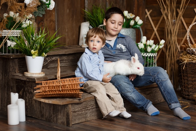 Two beautiful boys play with a white rabbit in a Studio with rustic decor. Funny and cute brothers