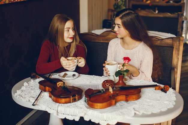 two beautiful elegant girls sitting in a cafe with violin and drinking coffee