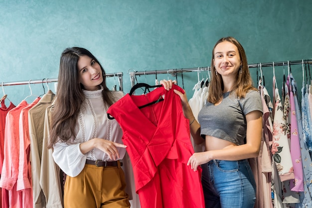 Photo two beautiful girlfriends choose a beautiful red dress for a ball in a stylish store