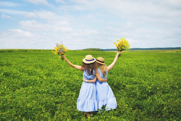 Two beautiful girlfriends in hats hugging in green field