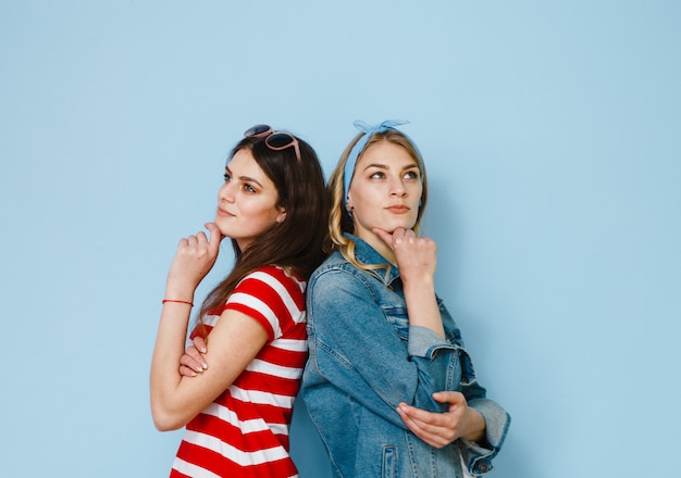 Two beautiful girlfriends have fun and show gestures on a blue background