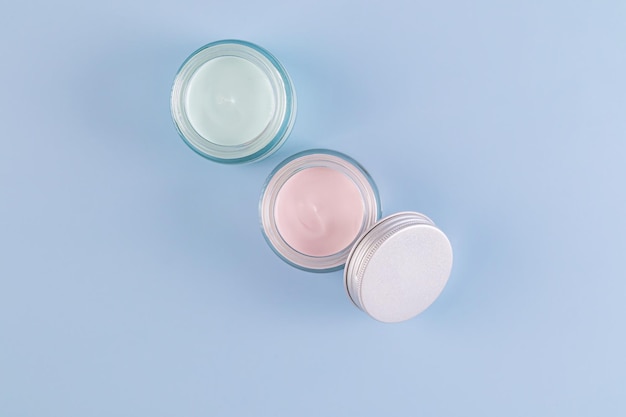 two beautiful glass cosmetic jars with delicate texture of face and body care cream on a blue background Top view A copy space presentation