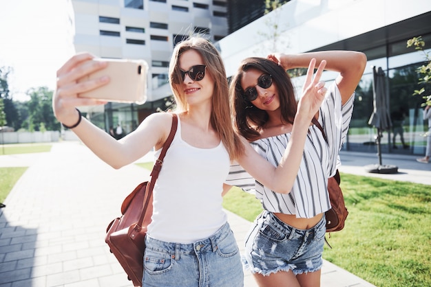 Two beautiful happy young student girl with backpack near the campus of university. Education and leisure concept