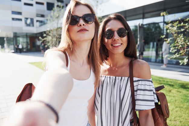 Two beautiful happy young student girl with backpack near the campus of university. Education and leisure concept