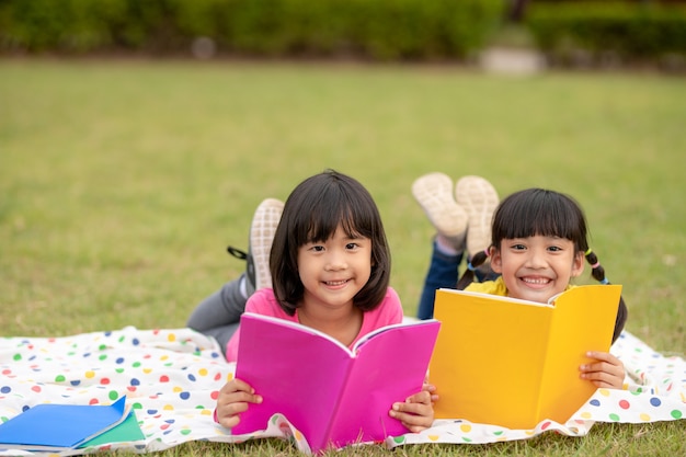 Two beautiful little girls reading books in the garden , sitting on grass. The concept of education and friendship.