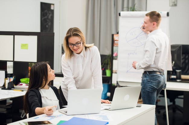 Two beautiful office workers having conversation while man colleague drawing business strategy on flip chart.