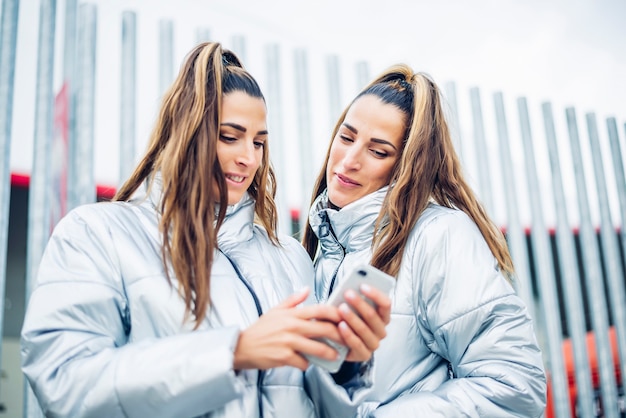 Two beautiful twin sisters using smartphone