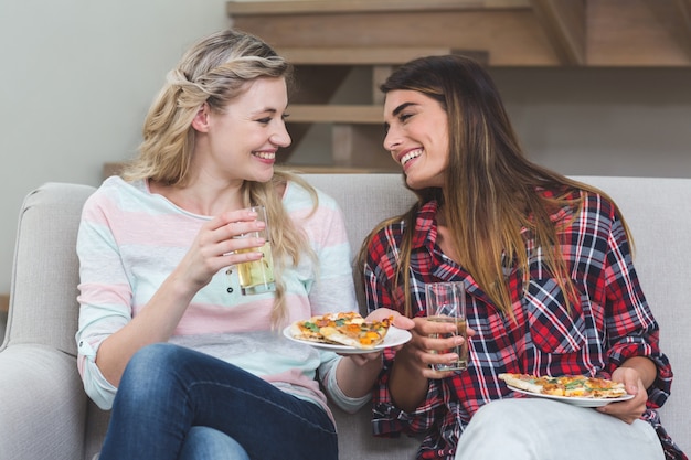 Two beautiful woman sitting on sofa and having pizza