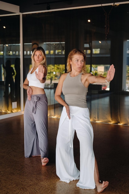 Two beautiful women are doing yoga standing up in the fitness room