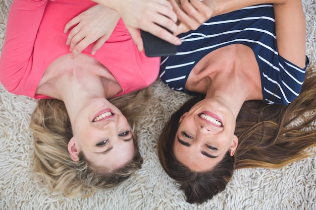 Two beautiful women lying on rug and looking at the mobile phone