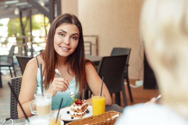 Two beautiful young girls sitting by the table in cafe