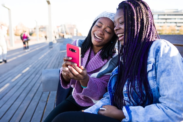 Two beautiful young woman using mobile phone in the street.