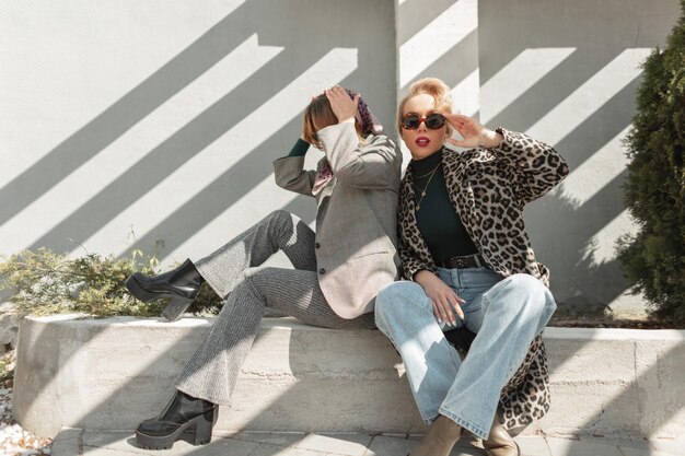 Photo two beautiful young women model with trendy clothes with shoes sits in the city