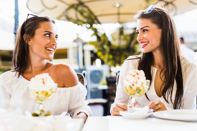 Two beautiful young women smiling and having a fruit salad in a restaraunt outdoors