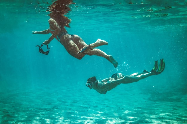 Two beautiful young women swim underwater enjoying the blue of the sea.